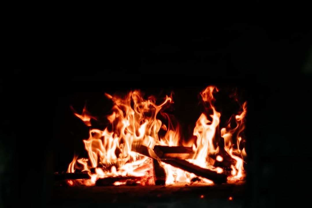Vor einem dunklen Hintergrund brennt ein Feuer mit leuchtend orangefarbenen Flammen, die Holzscheite verzehren und an einen Aachener Herd erinnern.