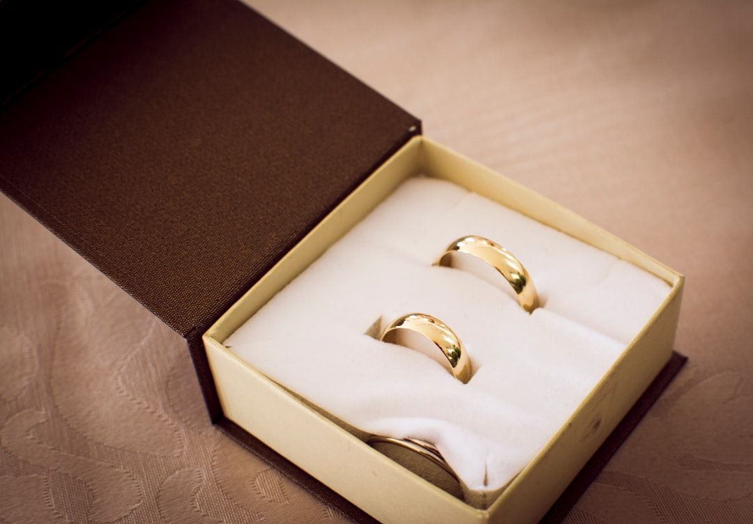 Zwei goldene Eheringe in einer gepolsterten Präsentationsbox, ein Ring etwas größer als der andere. Die Box, die an Aachener Handwerkskunst erinnert, ist außen dunkelbraun und innen hell gefärbt.
