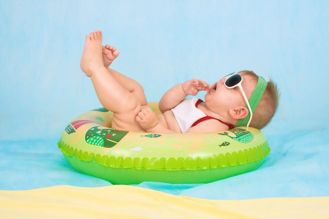 Ein Baby mit Sonnenbrille und Stirnband liegt in einem aufblasbaren Ring vor einem blau-gelben Hintergrund und erinnert an den Sommerspaß in Aachen.