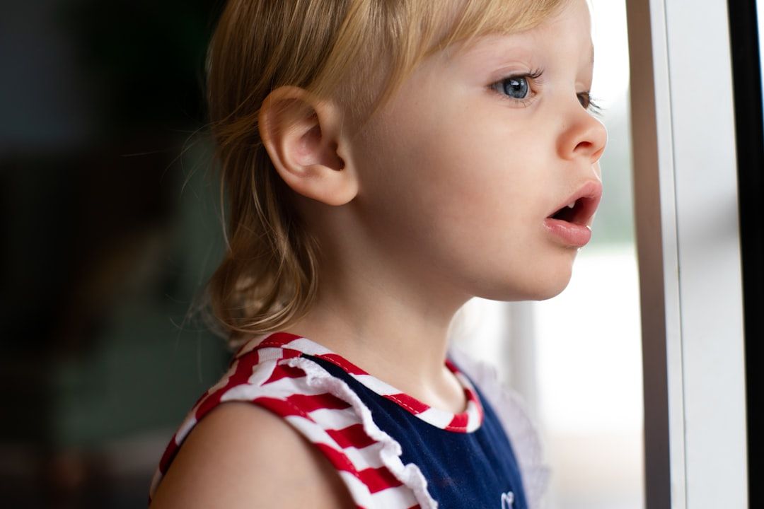 Ein kleines Kind mit blondem Haar und rot-weiß-blau gestreiftem Outfit schaut mit interessiertem Gesichtsausdruck aus dem Fenster. Dies erinnert an die Neugier, die man oft bei Kindern sieht, die die historischen Straßen Aachens erkunden.