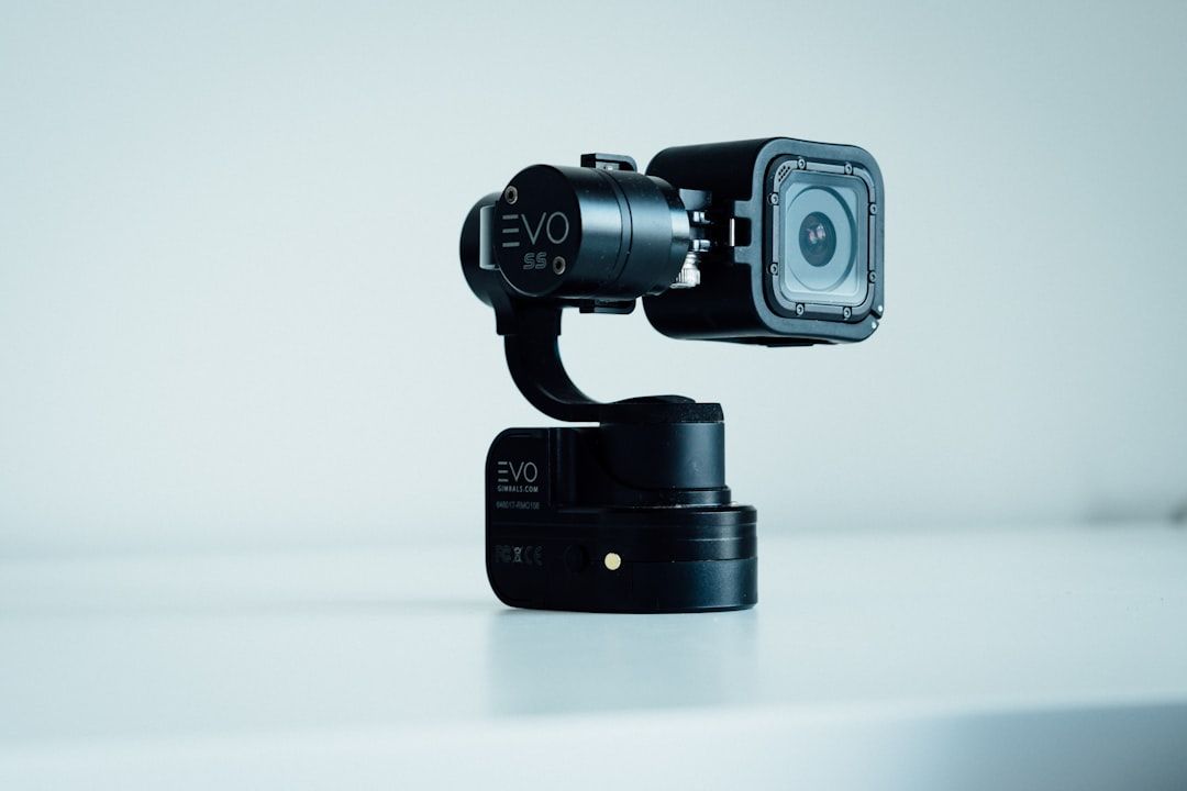 Ein schwarzer EVO SS-Kamera-Gimbal-Stabilisator mit einer darauf montierten Action-Kamera sitzt wie ein schlanker Wächter auf einer weißen Oberfläche und ist bereit, jeden malerischen Moment in Aachen festzuhalten.