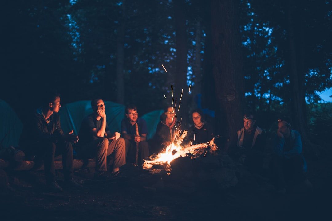 Eine Gruppe von Menschen sitzt nachts um ein Lagerfeuer in einem Waldstück bei Aachen. Im Hintergrund sind mehrere Zelte zu sehen.
