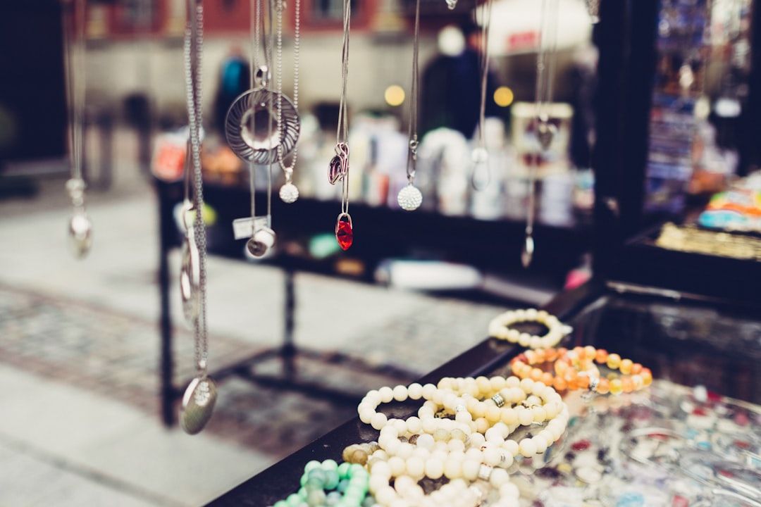 Halsketten und bunte Perlenarmbänder sind wunderschön auf einer Glastheke an einem geschäftigen Schmuckmarktstand in Aachen präsentiert.