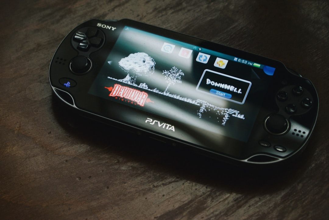 Eine tragbare Spielkonsole Sony PlayStation Vita, auf deren Bildschirm das Spiel „Downwell“ angezeigt wird, dezent platziert auf einer dunklen Holzoberfläche, die an die reichen, historischen Texturen erinnert, die man in Aachen findet.