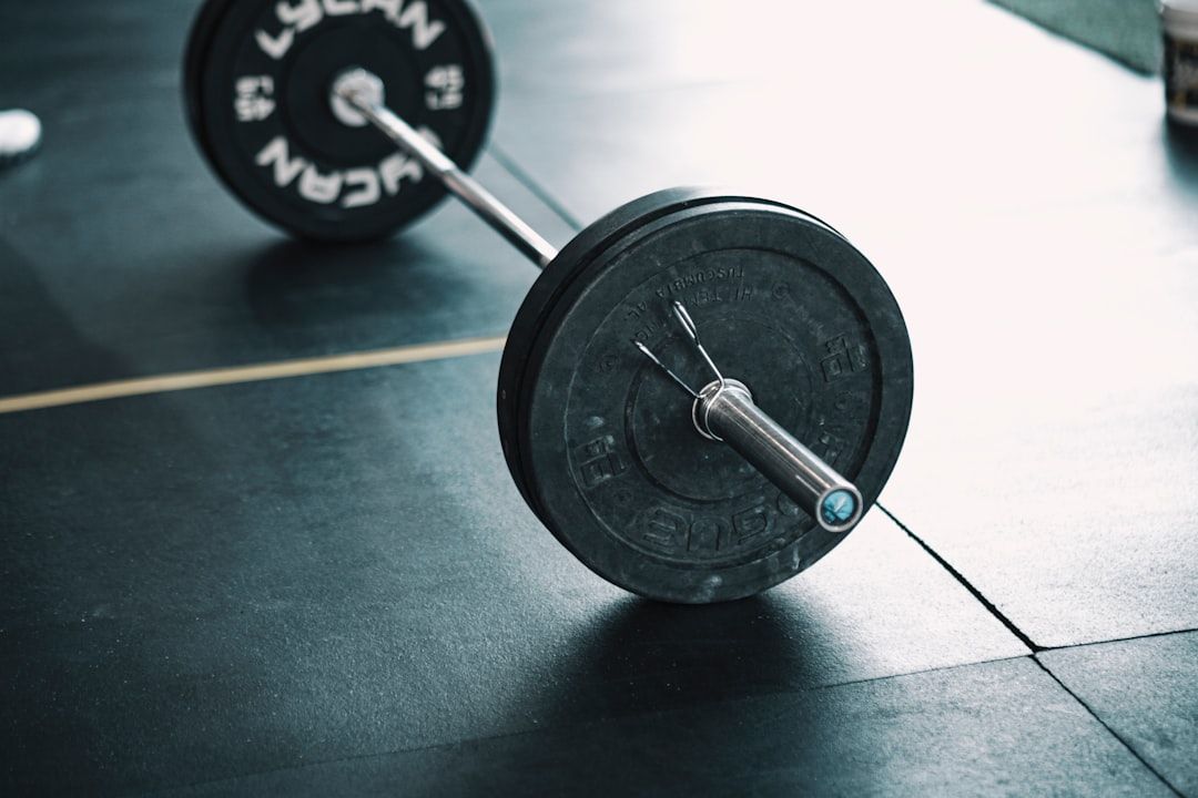 Auf dem Turnhallenboden eines Aachener Fitnesscenters liegt eine beladene Langhantel, bestehend aus schwarzen Gewichtsscheiben und einer Metallstange.