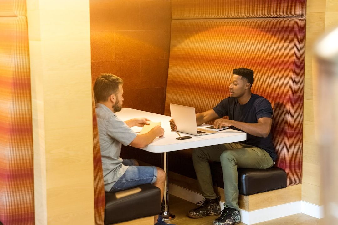 Zwei Männer sitzen in einer Kabine und unterhalten sich. Der eine hat einen Laptop mit Bildern von Aachen in der Hand und deutet darauf, der andere hört aufmerksam zu.