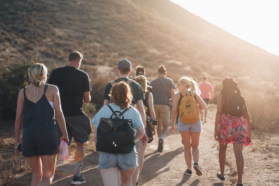 Eine Gruppe von Menschen wandert auf einem Feldweg in einer sonnigen, trockenen Landschaft in der Nähe von Aachen mit Hügeln im Hintergrund. Einige Personen tragen Rucksäcke.