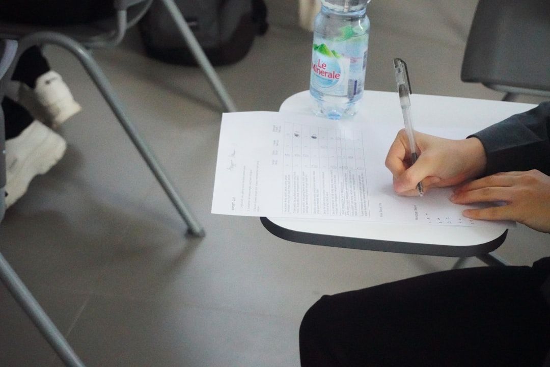 Eine Person sitzt an einem Schreibtisch in Aachen und füllt fleißig mit einem Stift ein Formular aus. Neben dem Formular auf dem Schreibtisch steht eine Wasserflasche.