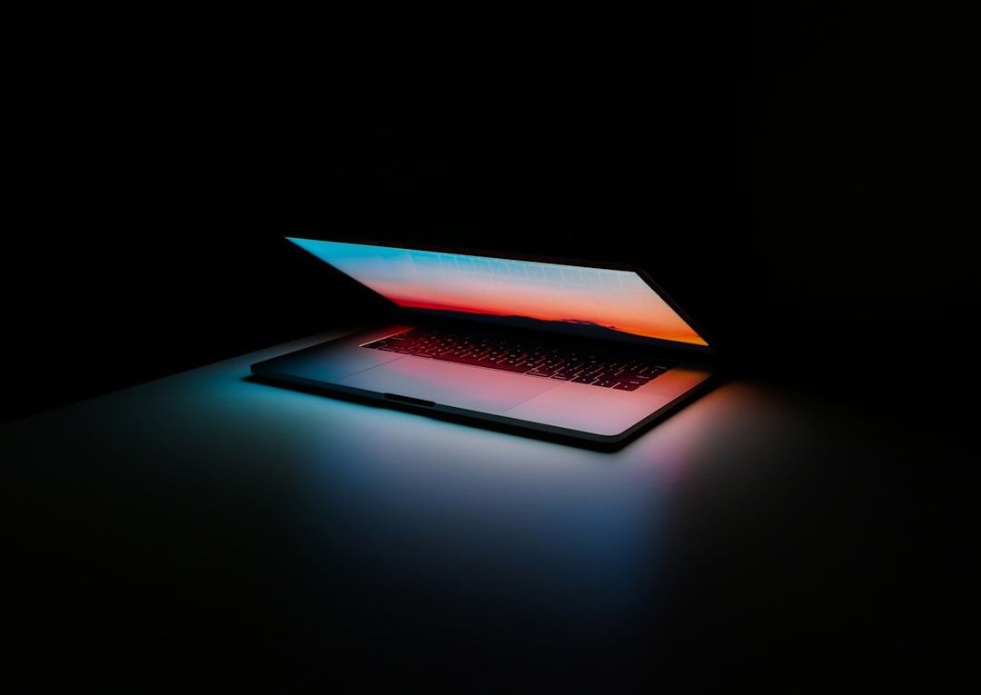 Ein teilweise geöffneter Laptop strahlt einen bunten Glanz von seinem Bildschirm aus und erhellt einen dunklen Raum, der an die pulsierenden Straßen von Aachen bei Nacht erinnert.