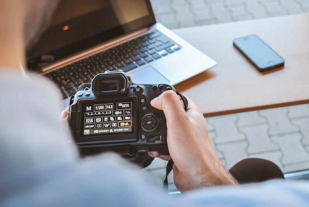 Eine Person in Aachen stellt eine Digitalkamera ein, im Hintergrund liegen Laptop und Smartphone auf dem Tisch.