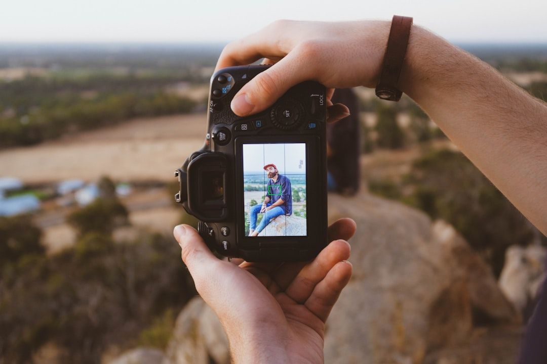 Eine Person hält eine Kamera und nimmt ein Bild einer anderen Person auf, die auf einem Felsen inmitten der Natur sitzt und an die bezaubernde Landschaft Aachens erinnert.