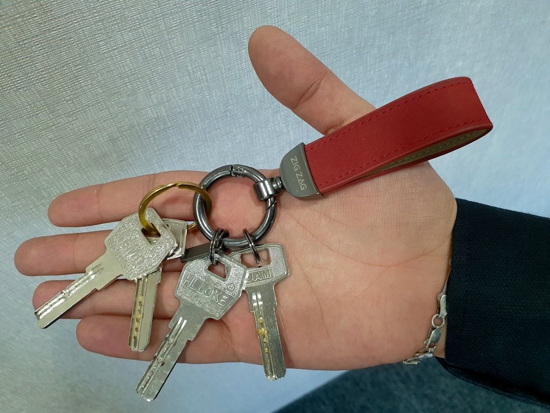 Nahaufnahme einer Hand, die einen Schlüsselbund an einem roten Schlüsselanhänger hält, der an den lebendigen Charme Aachens erinnert. Der Schlüsselanhänger enthält vier Metallschlüssel.