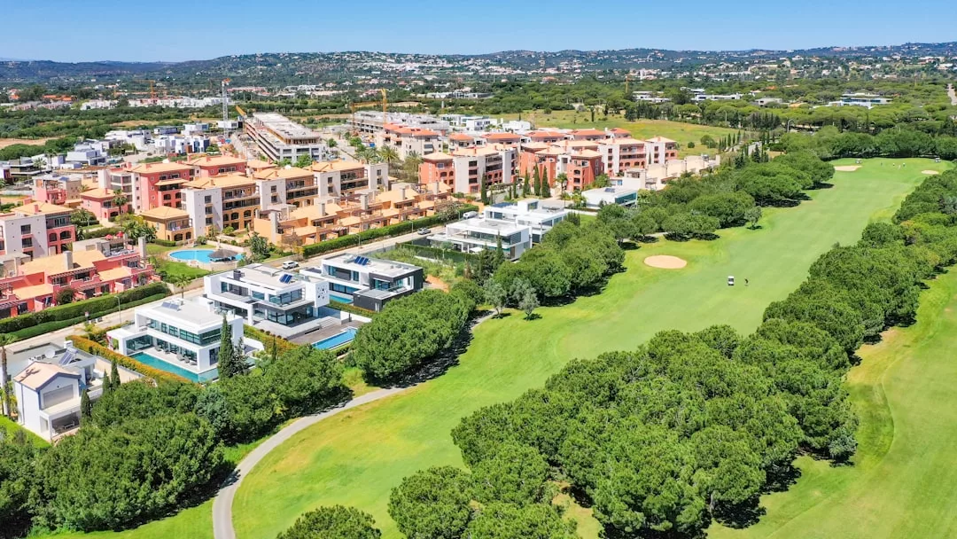 Luftaufnahme eines üppig grünen Golfplatzes mit Sandbunkern, gesäumt von modernen Wohngebäuden und umgeben von Bäumen unter einem klaren blauen Himmel.