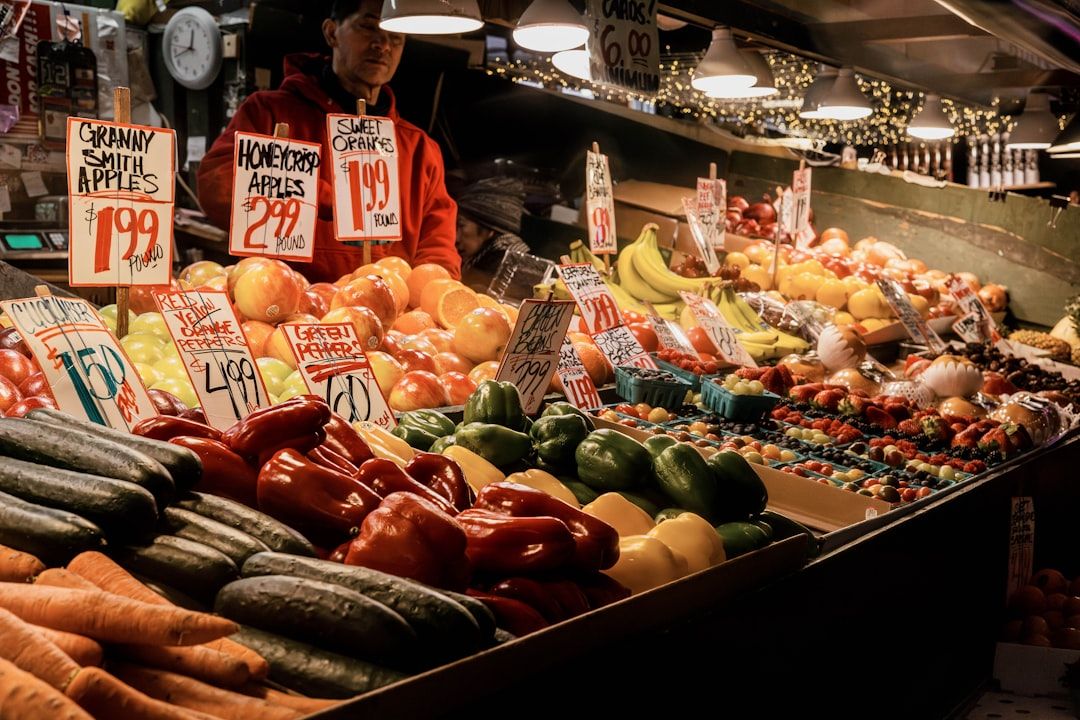 An einem Marktstand in Aachen werden verschiedene frische Produkte angeboten, darunter Paprika, Äpfel, Bananen und mehr. An den Verkaufsständen sind Preisschilder zu sehen, wie zum Beispiel Granny Smith-Äpfel für 1,99 $ und Honeycrisp-Äpfel für 2,99 $.
