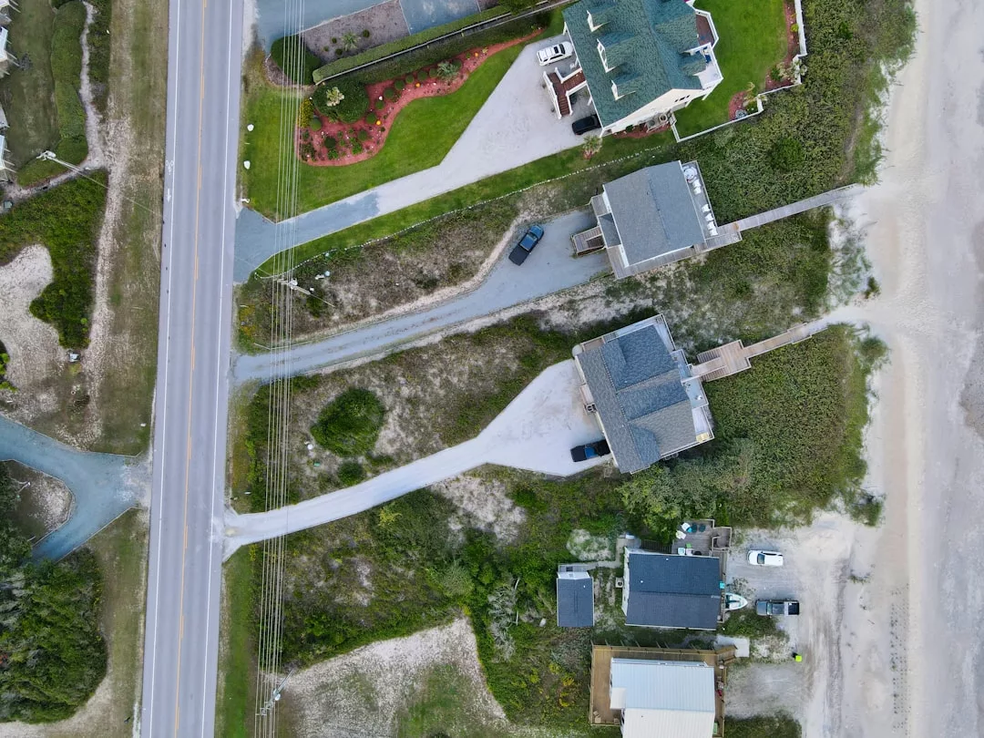 Luftaufnahme eines Küstenviertels mit Häusern, Straßen und Wegen, die zum Strand führen. Das Gebiet ist von Gras und Sanddünen umgeben.