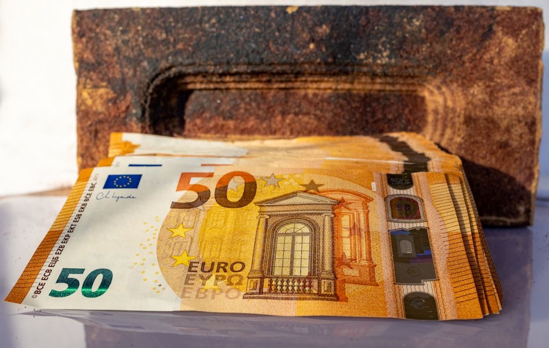 Fünfzig-Euro-Scheine liegen vor einem rostigen, rechteckigen Gegenstand, im Hintergrund ist ein Aachener Wahrzeichen zu sehen.