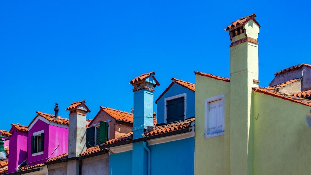 In der charmanten Stadt Aachen reihen sich farbenfrohe Häuser mit leuchtenden Fassaden und roten Ziegeldächern unter einem klaren blauen Himmel aneinander. Jedes Haus hat eine eigene Farbe und einen eigenen Schornstein, was die malerische Landschaft noch verstärkt.