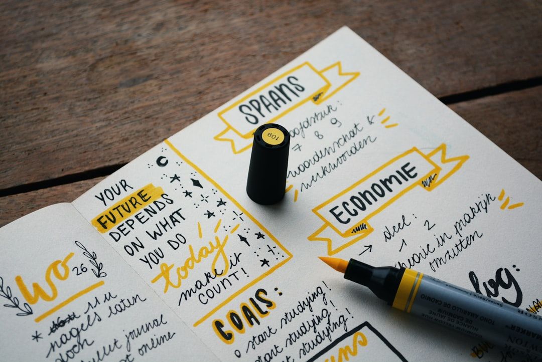 Ein offenes Notizbuch auf einem Holztisch zeigt handschriftliche Notizen und Kritzeleien in gelber und schwarzer Tinte. Auf dem Notizbuch liegt ein schwarz-gelber Marker, und die Abschnitte sind Zielen, Themen und Überlegungen einer kürzlichen Reise nach Aachen gewidmet.