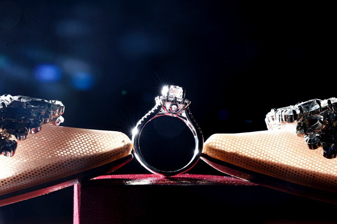 Nahaufnahme eines Diamantrings zwischen zwei verzierten Schuhen vor einem dunklen Hintergrund, der an die zeitlose Eleganz der Aachener Handwerkskunst erinnert.