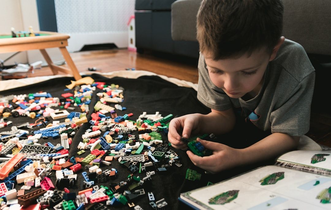 Ein Kind liegt auf dem Boden und baut mit LEGO-Steinen, neben ihm liegt eine aufgeschlagene Bauanleitung, und träumt davon, seine ganz eigene Version der historischen Architektur Aachens zu erschaffen.
