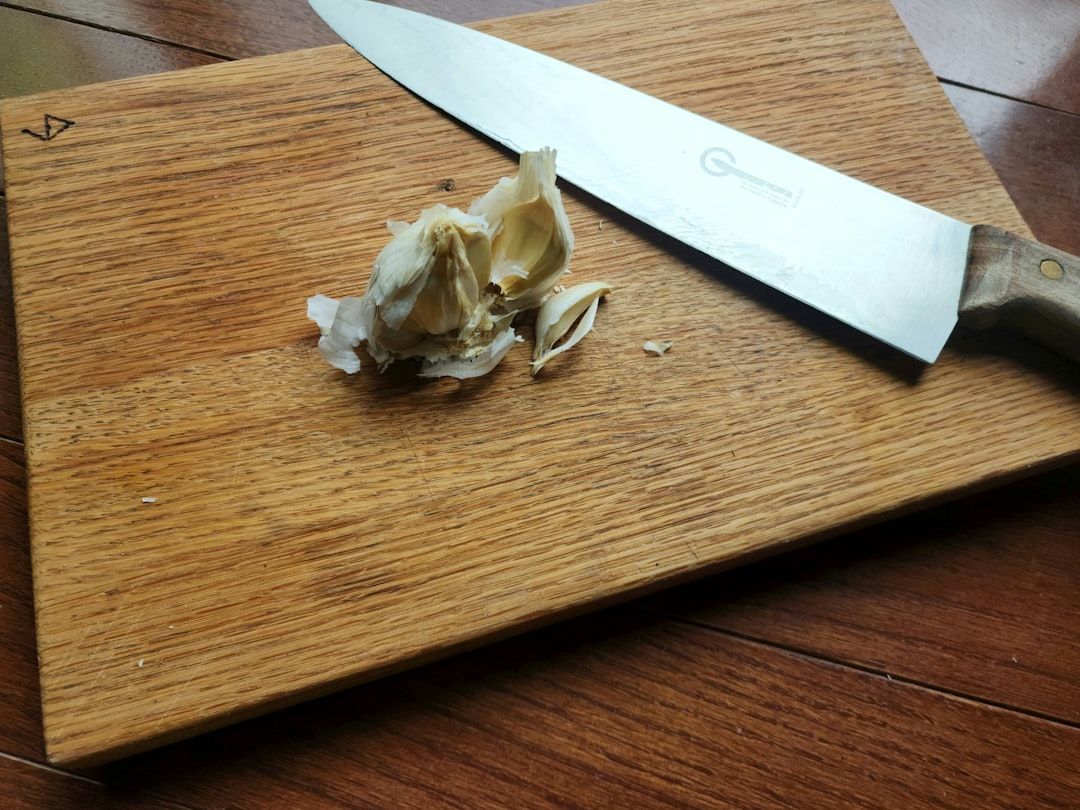 Ein Messer und eine aufgebrochene Knoblauchknolle liegen auf einem hölzernen Schneidebrett und erinnern an rustikale Küchen in Aachen.