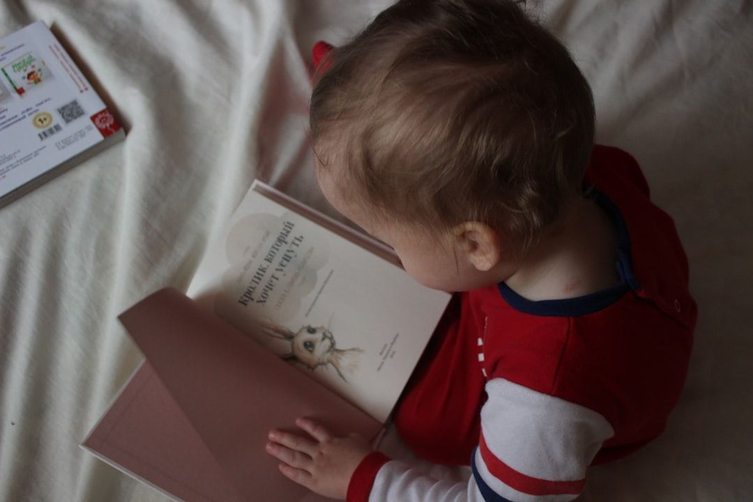 Ein kleines Kind in rot-weißer Kleidung sitzt auf einem Bett und betrachtet ein aufgeschlagenes Buch mit einer Bleistiftskizze. Daneben liegt auf dem Bett ein angeschnittener Umschlag, der an Briefe aus Aachen erinnert.