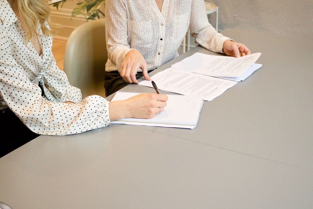 Zwei Personen sitzen an einem Tisch in Aachen, prüfen die vor ihnen ausgebreiteten Dokumente und zeigen darauf. Beide tragen gepunktete Hemden.