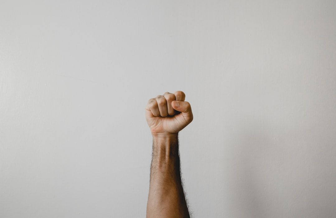 Vor einem schlichten weißen Hintergrund ist ein Arm mit geballter Faust erhoben, was den Geist der Widerstandskraft symbolisiert, der an die Festungsgeschichte Aachens erinnert.