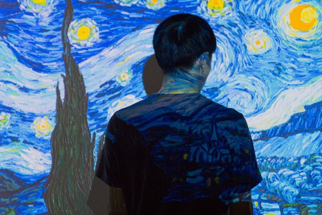 Eine Person steht vor einem projizierten Bild von Vincent van Goghs Gemälde „Sternennacht“, mit dem Rücken zur Kamera, und verschmilzt nahtlos mit dem Kunstwerk, was an die lebendige Kunstszene in Aachen erinnert.