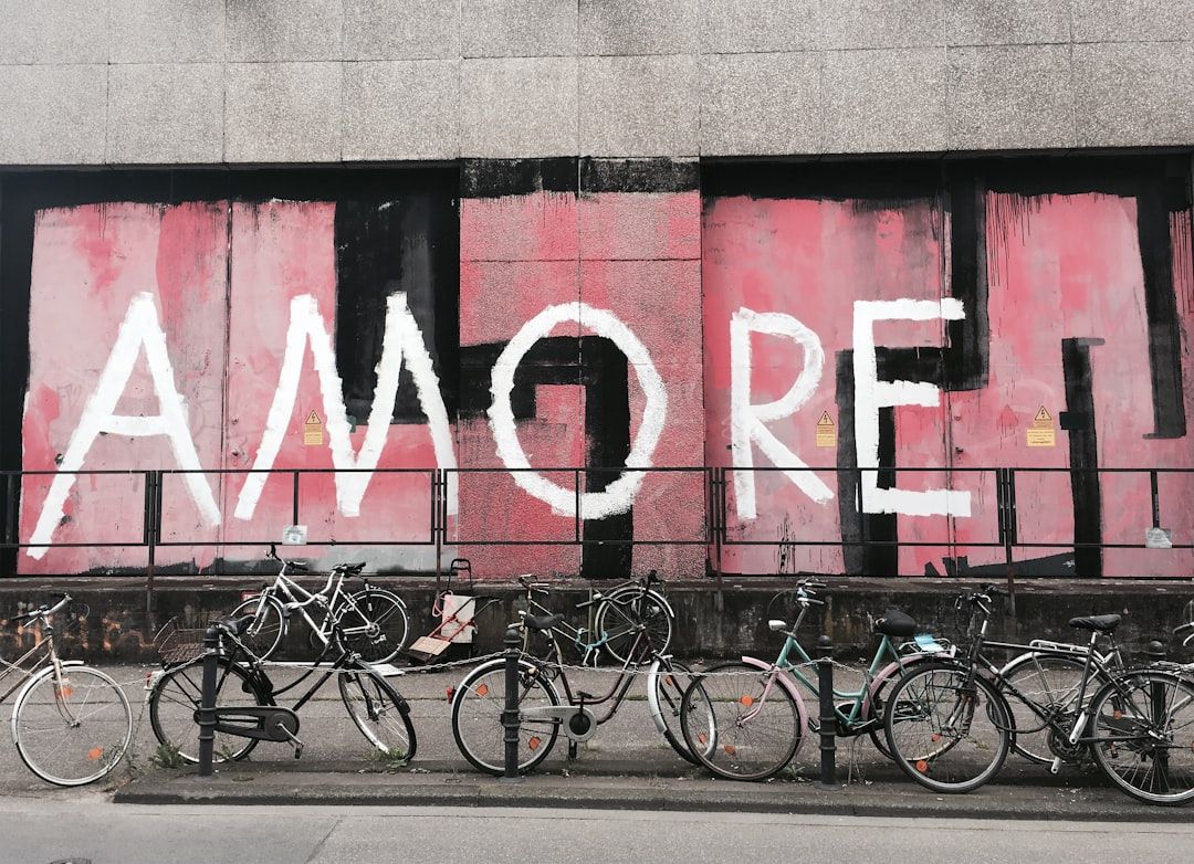 Eine Reihe abgestellter Fahrräder vor einem großen Graffiti auf einer grauen Wand. Auf dem Graffiti steht in weißen Lettern auf rosa Hintergrund „AMORE“ und erinnert damit an die lebendige Straßenkunst, die man überall in Aachen findet.