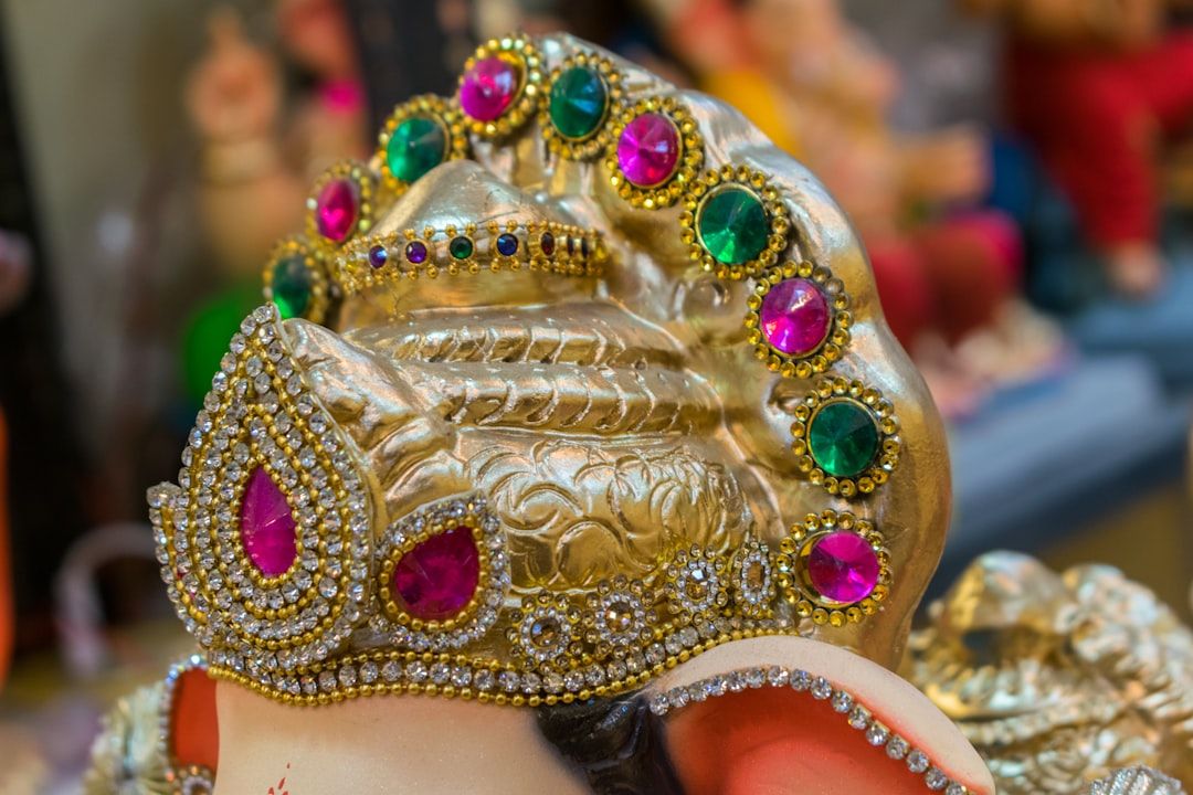 Nahaufnahme eines mit Gold und rosafarbenen und grünen Edelsteinen verzierten Kopfschmucks, Teil einer Ganesha-Skulptur, die an die komplexe Kunstfertigkeit Aachens erinnert.