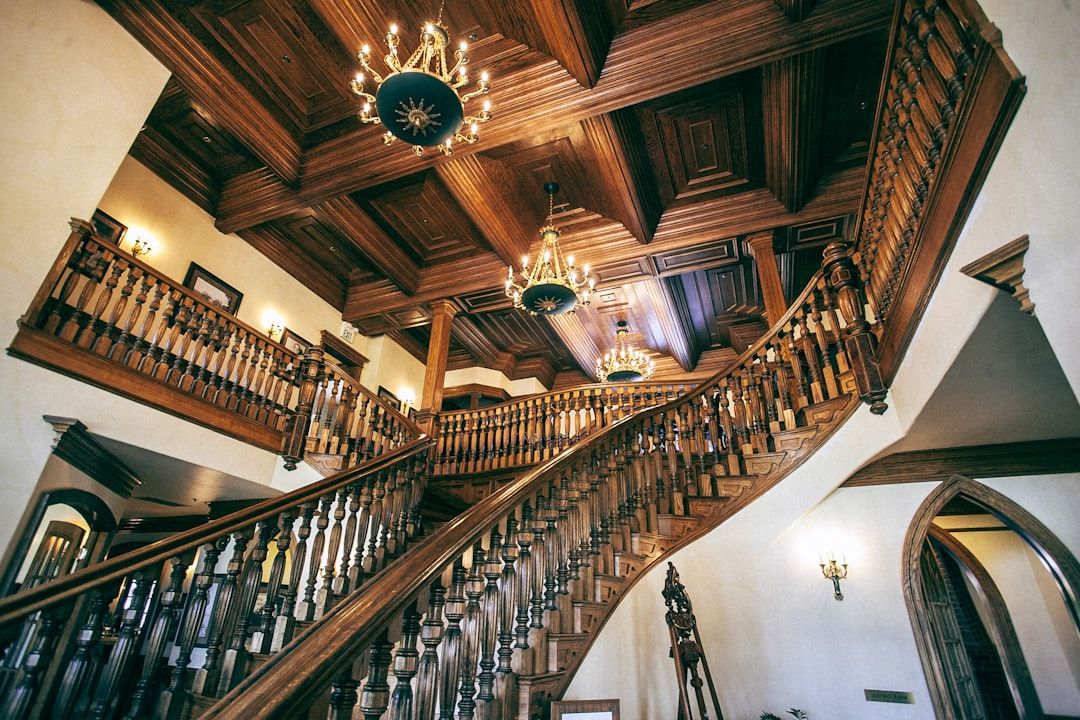 Eine große, hölzerne Doppeltreppe mit aufwendigem Geländer in einer kunstvoll verzierten Halle mit Kronleuchtern und Kassettendecke, die an die Eleganz der historischen Architektur Aachens erinnert.