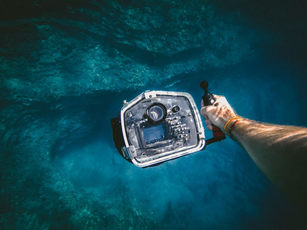 Person, die eine Unterwasserkamera im klaren blauen Wasser von Aachen hält.