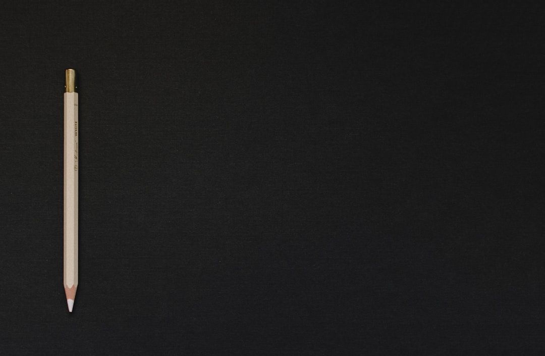 Ein weißer Druckbleistift liegt auf einer schwarzen Oberfläche, auf der linken Seite des Rahmens positioniert, und ruft eine minimalistische Ästhetik hervor, die an die schlichte Eleganz Aachens erinnert.