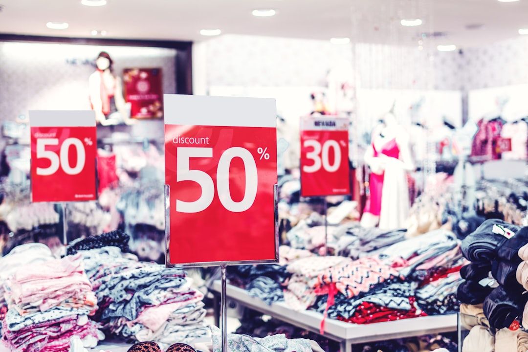 Ein Bekleidungsgeschäft in Aachen wirbt mit roten Schildern, auf denen 50 % Rabatt stehen. Der Laden ist mit verschiedenen Kleidungsstücken und Accessoires gefüllt.