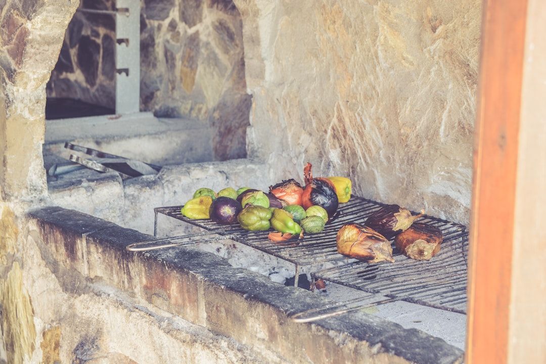 Ein Steinofen mit Metallgrill, auf dem Gemüse wie Paprika und Zwiebeln gegrillt werden, erinnert an die rustikalen Küchen Aachens. Im Hintergrund sind Kochutensilien zu sehen.