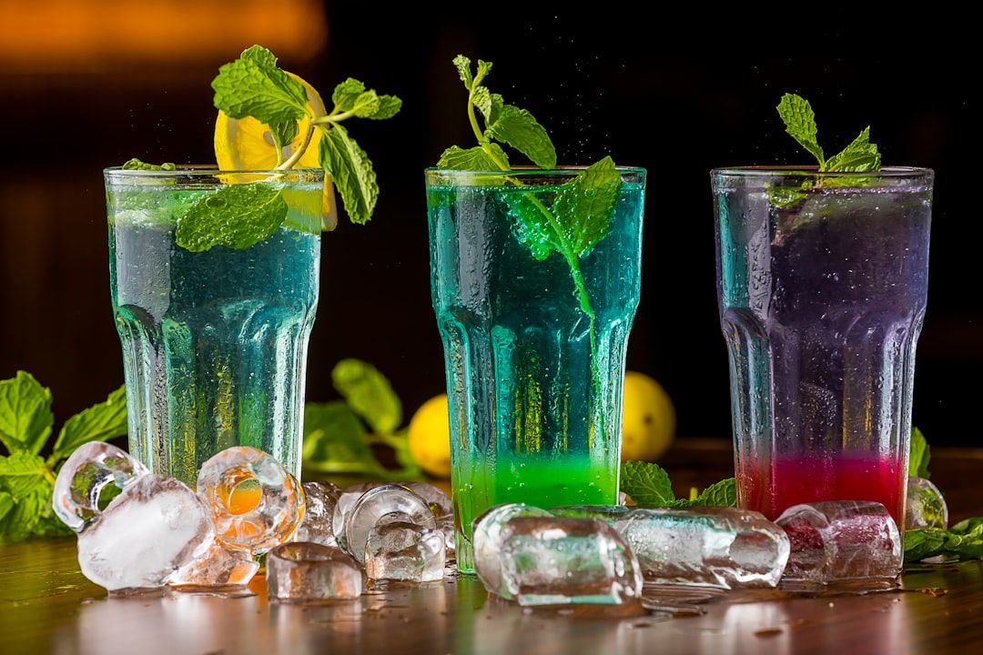 Drei spritzige Cocktails, garniert mit Minzblättern und Zitronenscheiben, begleitet von verstreuten Eiswürfeln auf einem Holztisch, laden Sie zu einer erfrischenden Auszeit ein, die an einen Abend in Aachen erinnert.