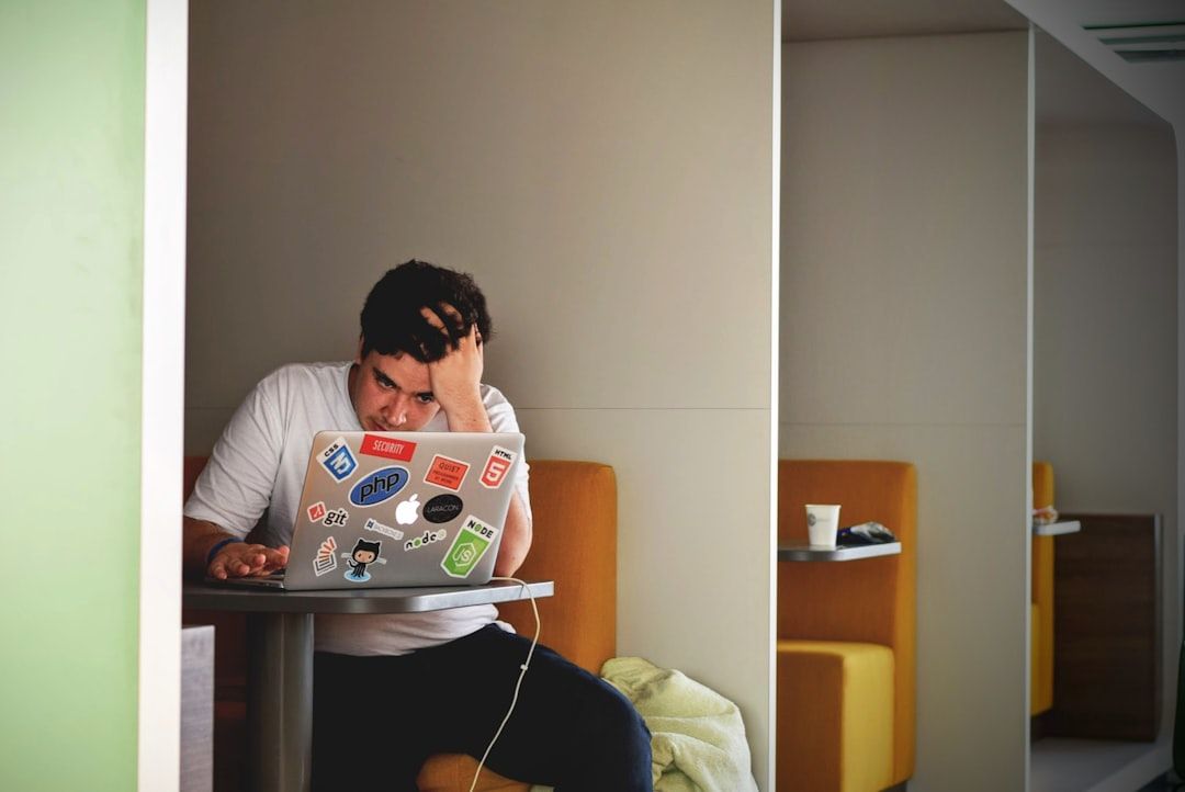 Eine Person sitzt an einem Tisch und arbeitet konzentriert an einem mit Aufklebern bedeckten Laptop. Mit einer Hand hält sie den Kopf, während sie komplexe Aufgaben erledigt – vielleicht lässt sie sich dabei von ihrer Zeit in Aachen inspirieren.