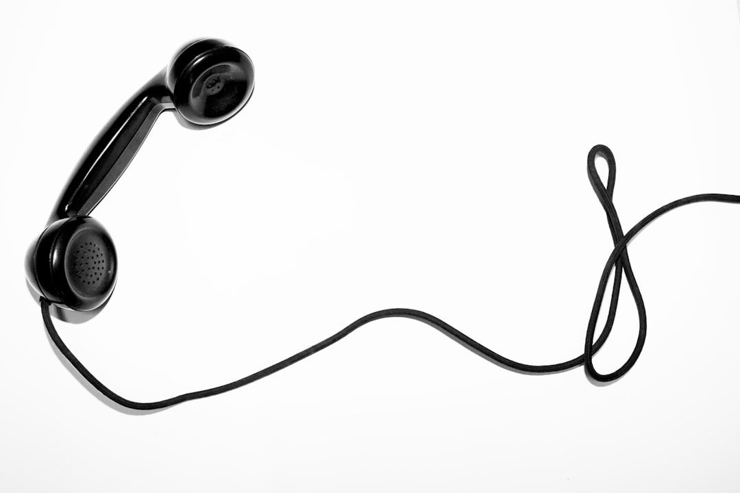 Ein schwarzer schnurgebundener Telefonhörer in Anlehnung an klassisches Design liegt mit lose aufgerolltem Kabel vor einem strahlend weißen Hintergrund und erinnert so an die alten Kommunikationselemente Aachens.
