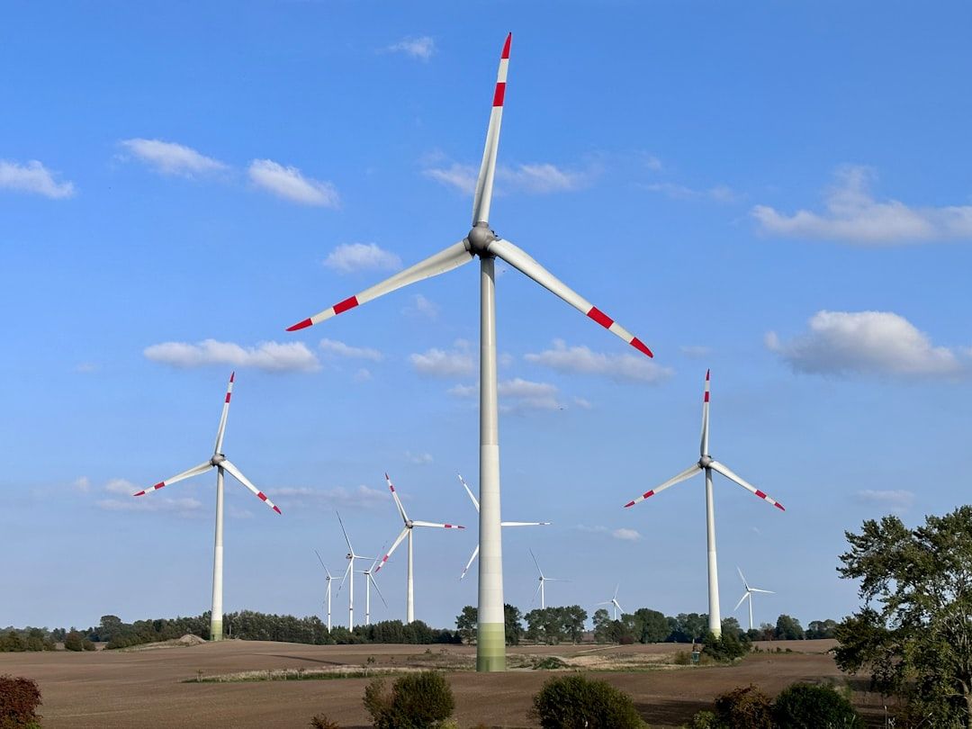 Auf einem Feld in der Nähe von Aachen sind mehrere Windräder unter einem blauen Himmel mit vereinzelten Wolken zu sehen.