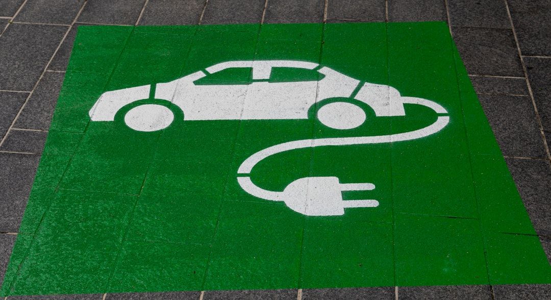 Grünes Parkplatzschild in Aachen mit dem weißen Umriss eines an eine Ladesteckdose angeschlossenen Elektroautos.