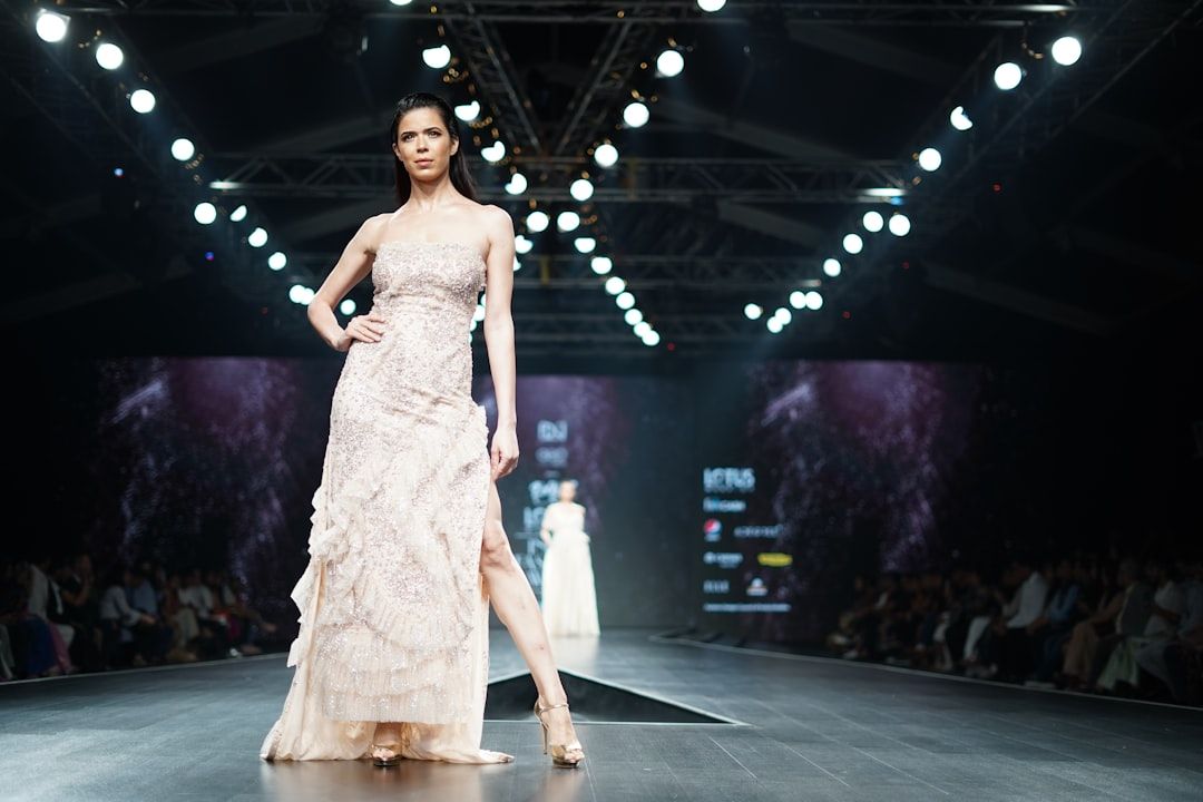 Ein Model im hellen Abendkleid läuft während der renommierten Aachener Modenschau über den Laufsteg, im Hintergrund Publikum und beleuchtete Kulisse.