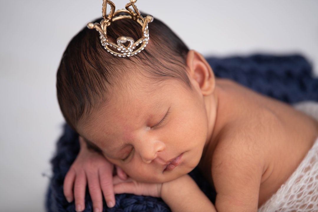 Ein neugeborenes Baby schläft friedlich mit einer kleinen dekorativen Krone auf dem Kopf und liegt auf einer dunkelblauen Decke, die an das königliche Erbe in Aachen erinnert.