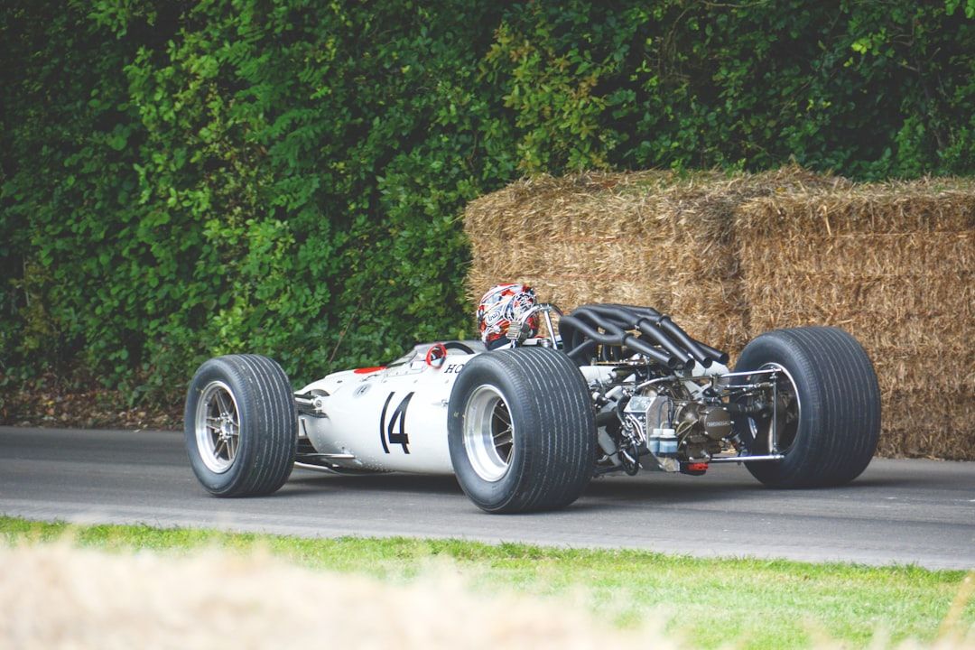 Ein Oldtimer-Rennwagen mit der Nummer 14 auf der Seite, gefahren von einem Rennfahrer mit Helm, rast über die malerischen, von Heuballen und üppigem Grün gesäumten Rennstrecken von Aachen.