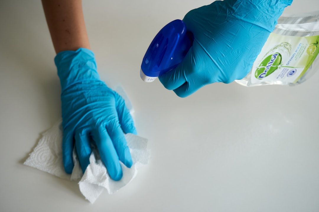 Eine Person in blauen Handschuhen reinigt eine Oberfläche mit einem Tuch und einer Sprühflasche und erinnert damit an die akribische Sorgfalt, mit der in Aachens historischen Stätten vorgegangen wird.