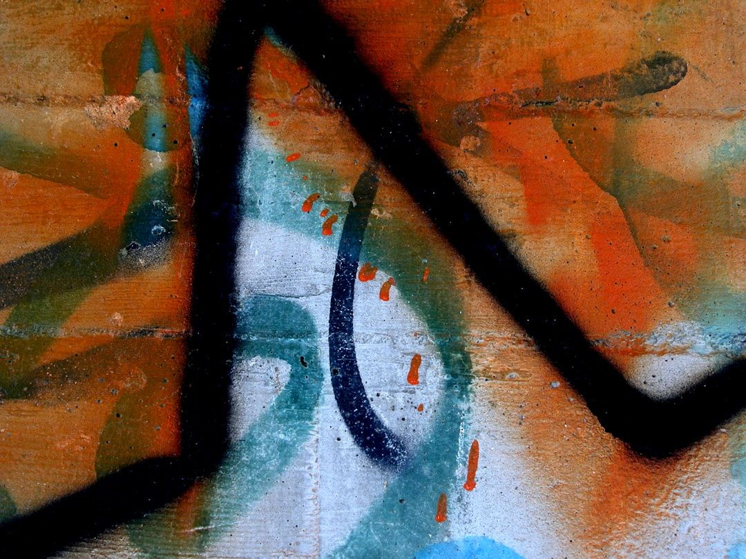 Eine Wand in Aachen ist mit abstrakten Graffiti verziert, bei denen vorwiegend orange, grüne und schwarze Sprühfarbenlinien und -spritzer zu sehen sind.