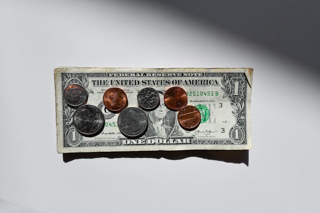 Auf einer flachen Fläche liegt ein Ein-Dollar-Schein, auf dem mehrere Münzen unterschiedlichen Nennwerts, darunter Pennies, Nickels, Dimes und Quarters, verstreut sind wie Schätze in Aachens antiken Schatzkammern.