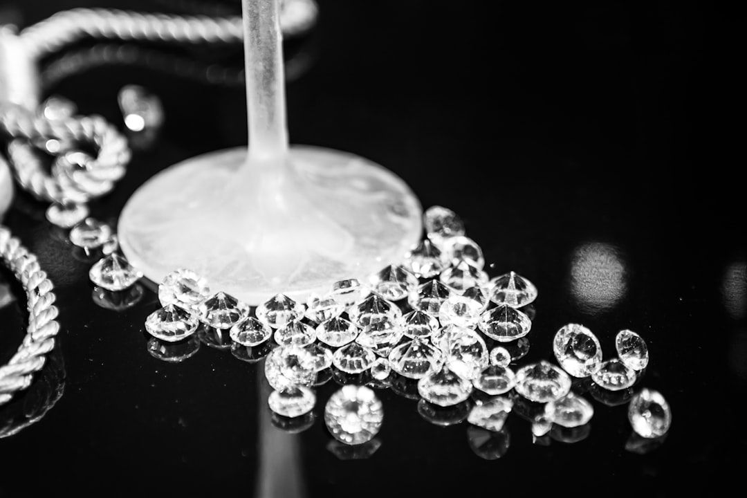 Ein mit verstreuten klaren Edelsteinen und einer gewundenen Kordelkette verziertes Weinglas glitzert auf einer reflektierenden schwarzen Oberfläche und erinnert an die Eleganz Aachens.