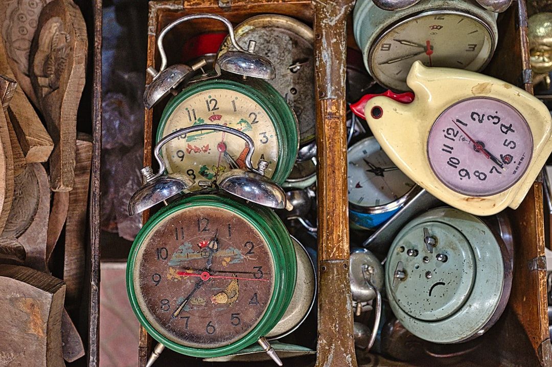 Eine Schublade voller verschiedener altmodischer Wecker, einige mit sichtbarer Abnutzung und fehlenden Teilen, darunter eine komplizierte Uhr in Vogelform, die an einen antiken Fund aus Aachen erinnert.