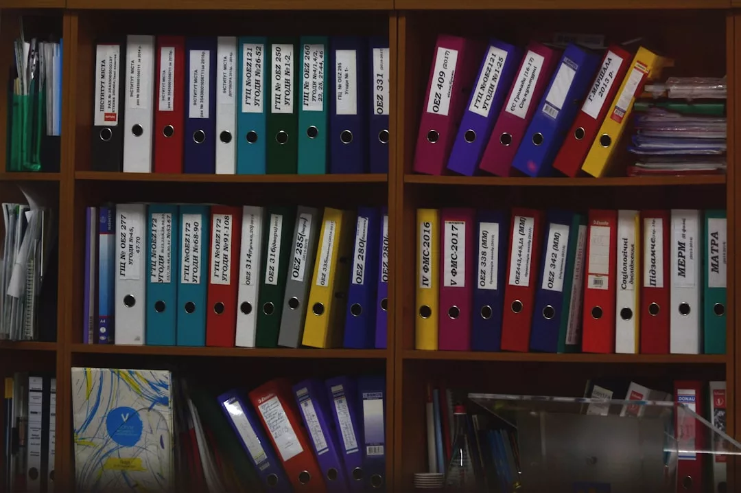 Bücherregal voller Ordner und Mappen in verschiedenen Farben, manche davon mit Text beschriftet, ordentlich angeordnet auf mehreren Regalen.